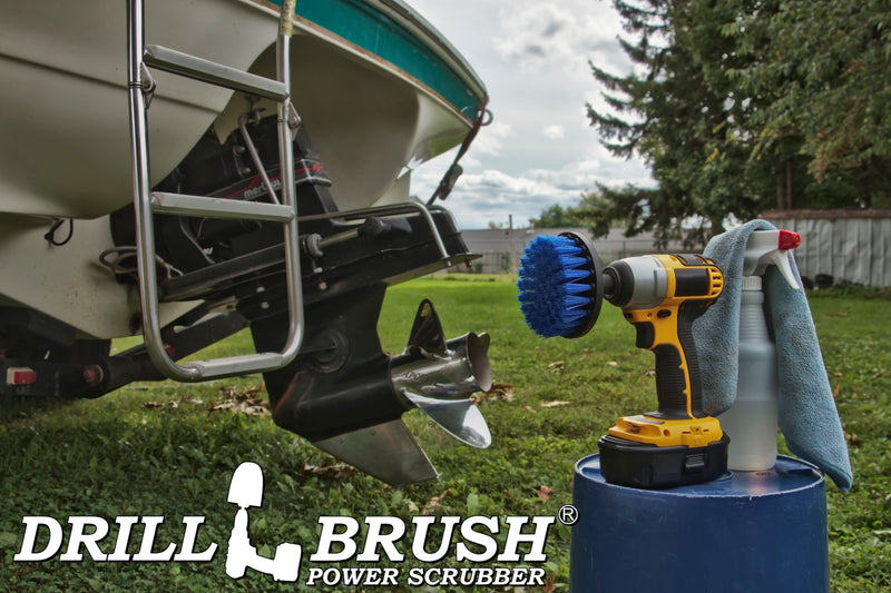Drillbrush 4 inch Medium Blue Marine & Pool Brush in a cordless drill on a bucket next to a spray bottle and rag in front of a boat on a trailer in a backyard.