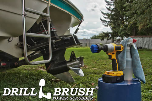 Drillbrush 2 inch Short Medium Blue Marine & Pool Brush in a cordless drill on a bucket next to a spray bottle and rag in front of a boat on a trailer in a backyard.