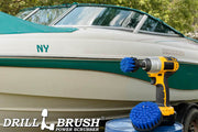 The Drillbrush 42 Medium Blue Marine & Pool Brush Kit in a cordless drill sitting on a bucket in front of a boat on a trailer in a backyard.