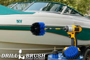 The Drillbrush 42O-5X Medium Blue Marine & Pool Brush Kit in a cordless drill sitting on a bucket in front of a boat on a trailer.
