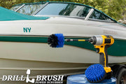 The Drillbrush 4M-5X Medium Blue Marine & Pool Brush Kit in a cordless drill sitting on a bucket in front of a boat on a trailer.