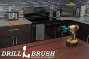 Drillbrush Mini Medium Green Kitchen Brush on a table in front of a kitchen counter, stove, microwave, and other appliances.