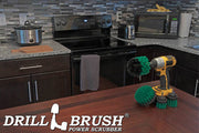 The Drillbrush 42OS-2L Medium Green Kitchen Brush Kit in a cordless drill sitting on a dinner table in front of kitchen counters, a stove, a toaster, and a microwave.