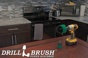 The Drillbrush 2O Medium Green Kitchen Brush Kit in a cordless drill sitting on a dinner table in front of kitchen counters, a stove, a toaster, and a microwave.