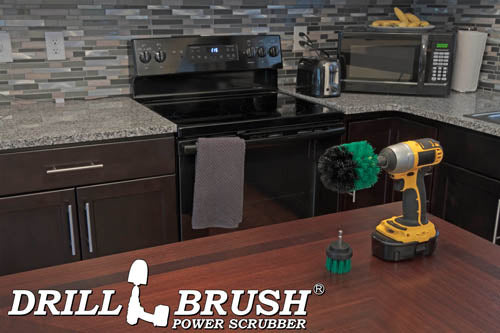 The Drillbrush 2O Medium Green Kitchen Brush Kit in a cordless drill sitting on a dinner table in front of kitchen counters, a stove, a toaster, and a microwave.