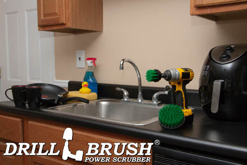 The Drillbrush 42 Medium Green Kitchen Brush Kit in a cordless drill sitting on a kitchen counter in front of a sink, coffeemaker, and dishes.