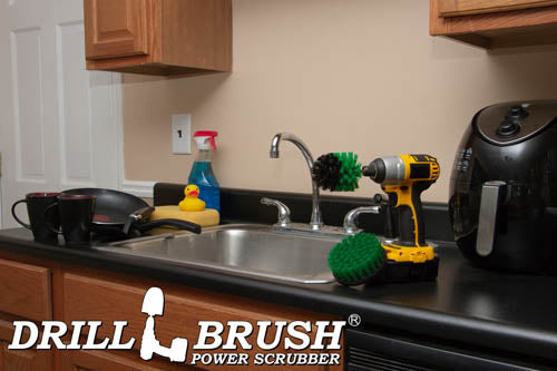 The Drillbrush 4M Medium Green Kitchen Brush Kit in a cordless drill sitting on a countertop in front of a sink, coffeemaker, and dishes.
