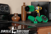 The Drillbrush 542O Medium Green Kitchen Brush Kit in a cordless drill sitting on a counter next to a stove in front of a microwave and decorative vases.