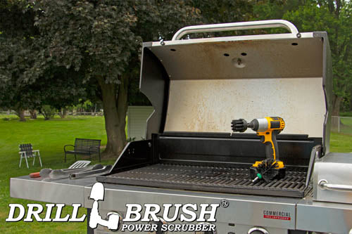 The Drillbrush 2M Ultra Stiff Black Grill & Industrial Brush Kit in a cordless drill sitting on an open grill in front of a grassy backyard.