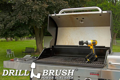 The Drillbrush 2O Ultra Stiff Black Grill & Industrial Brush Kit in a cordless drill sitting on an open grill in front of a grassy backyard.