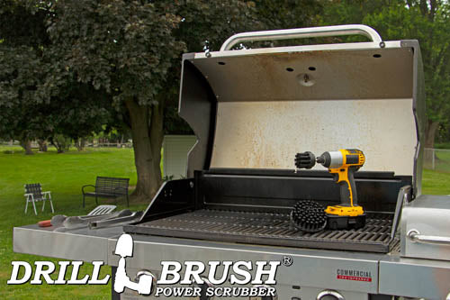 The Drillbrush 42 Ultra Stiff Black Grill & Industrial Brush Kit in a cordless drill sitting on an open grill in front of a grassy backyard.