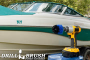 Drillbrush Mini Medium Blue Marine & Pool Brush in a cordless drill on a bucket next to a spray bottle and rag in front of a boat on a trailer in a backyard.