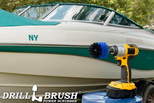 Drillbrush Mini Medium Blue Marine & Pool Brush in a cordless drill on a bucket next to a spray bottle and rag in front of a boat on a trailer in a backyard.