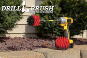 The Drillbrush 4M-5X Red Stiff Outdoor & Patio Brush Kit in a cordless drill sitting on a brick planter in front of a rock garden and some shrubs.