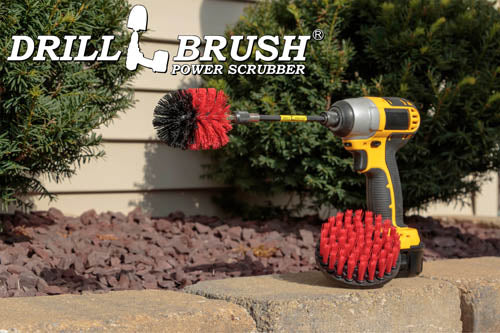 The Drillbrush 4M-5X Red Stiff Outdoor & Patio Brush Kit in a cordless drill sitting on a brick planter in front of a rock garden and some shrubs.