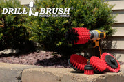 The Drillbrush E542J Red Stiff Outdoor & Patio Brush Kit in a cordless drill sitting on a brick planter in front of some shrubs.