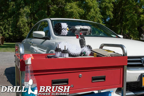 The Drillbrush 542OMS-2L Soft White Home & Auto Brush Kit in a cordless drill sitting on a tool cart in front of a white sedan.