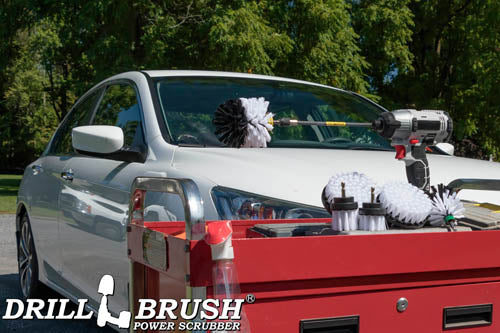 The Drillbrush 542OMS-2L-7X Soft White Home & Auto Brush Kit in a cordless drill sitting on a tool cart in front of a white sedan.