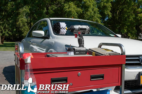 The Drillbrush 2O Soft White Home & Auto Brush Kit in a cordless drill sitting on a tool cart in front of a white sedan.