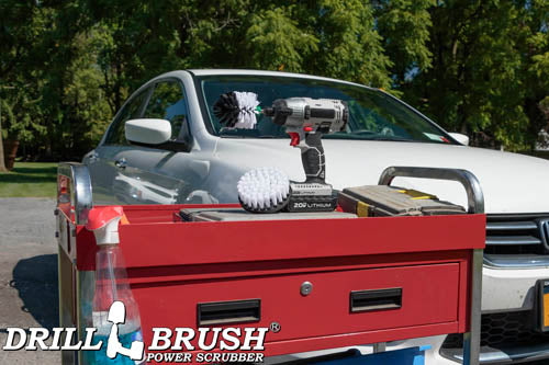 The Drillbrush 4M Soft White Home & Auto Brush Kit in a cordless drill sitting on a tool cart in front of a white sedan.