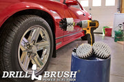 The Drillbrush 542O Soft White Home & Auto Brush Kit in a cordless drill sitting on a bucket next to a spray bottle and a rag in front of a red sports car.