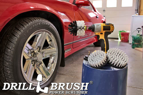 The Drillbrush 542O Soft White Home & Auto Brush Kit in a cordless drill sitting on a bucket next to a spray bottle and a rag in front of a red sports car.