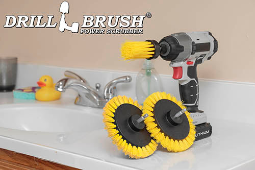 2 Drillbrush Medium Yellow Bathroom Edge brushes and a Medium Yellow 1 inch Long brush in a cordless drill on a bathroom counter.