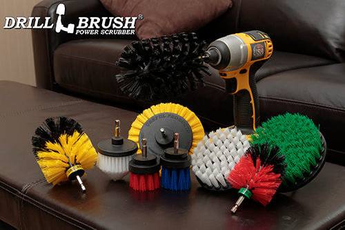 The Drillbrush 9-piece kit featuring Soft White Cone and 4 inch brushes, Medium Yellow Edge and Original brushes, Medium Green 5 inch brush, Medium Blue 2 inch Long brush, Stiff Red 2 inch Short and Mini Original brushes, and Ultra Stiff Jumbo Original brush on a living room coffee table.