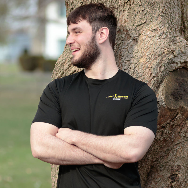 Model wearing the Drillbrush black polyester t-shirt in a public setting.