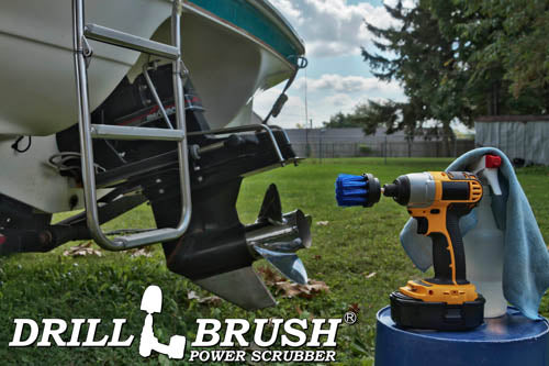 Drillbrush 2 inch Long Medium Blue Marine & Pool Brush in a cordless drill on a bucket next to a spray bottle and rag in front of a boat on a trailer in a backyard.