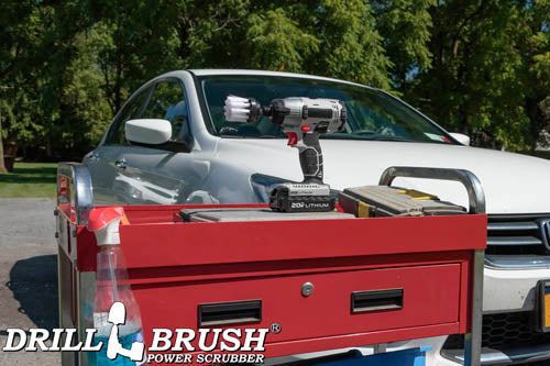 Drillbrush 2 inch Short Soft White Home & Auto Brush in a cordless drill on a tool cart in front of a white sedan.
