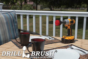 Drillbrush 2 inch Short Stiff Red Outdoor & Patio Brush on a deck table next to paper plates, silverware, and mugs in front of a backyard.