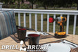 Drillbrush 2 inch Short Stiff Red Outdoor & Patio Brush on a deck table next to paper plates, silverware, and mugs in front of a backyard.