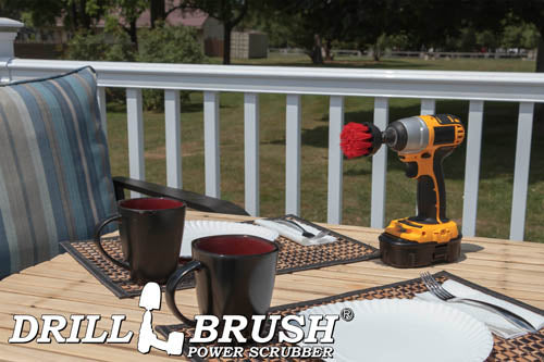 Drillbrush 2 inch Short Stiff Red Outdoor & Patio Brush on a deck table next to paper plates, silverware, and mugs in front of a backyard.
