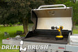 Drillbrush 2 inch Short Ultra Stiff Black Grill & Industrial Brush in a cordless drill on an open grill in front of a backyard.