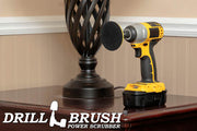 The Drillbrush 3in Hook-and-Loop Pad Backer in a cordless drill on a wooden end table in front of a lamp.
