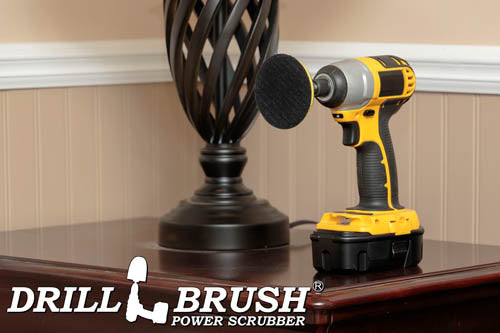 The Drillbrush 3in Hook-and-Loop Pad Backer in a cordless drill on a wooden end table in front of a lamp.