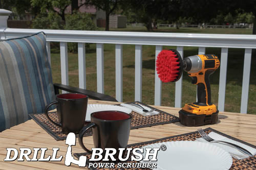 Drillbrush 4 inch Stiff Red Outdoor & Patio Brush on a deck table next to paper plates, silverware, and mugs in front of a backyard.