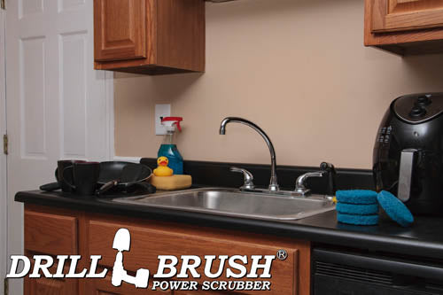The Drillbrush Stiff Blue 4 inch Scrubbing Pad Refill Kit in a stack on a kitchen counter in front of a sink, dishes, and a coffeemaker.