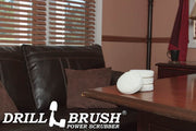 The Drillbrush Soft White 4 inch Scrubbing Pad Refill Kit in a stack on a wooden desk in front of a leather sofa in a personal office.