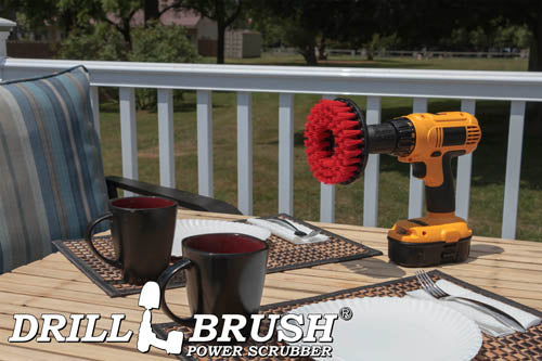 Drillbrush 5 inch Hex Stiff Red Outdoor & Patio Brush on a deck table next to paper plates, silverware, and mugs in front of a backyard.