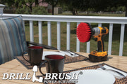 Drillbrush 5 inch Stiff Red Outdoor & Patio Brush on a deck table next to paper plates, silverware, and mugs in front of a backyard.