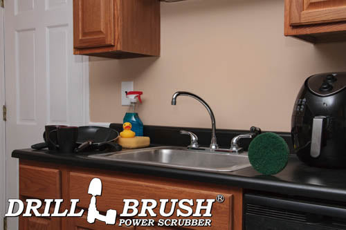The Drillbrush Abrasive Green 5 inch Scrubbing Pad on a kitchen counter in front of a sink, dishes, and a coffeemaker.