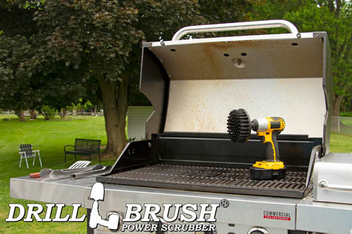 Drillbrush 5 inch Ultra Stiff Black Grill & Industrial Brush in a cordless drill on an open grill in front of a backyard.