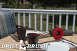 Drillbrush 5 inch Threaded Stiff Red Outdoor & Patio Brush on a deck table next to paper plates, silverware, and mugs in front of a backyard.