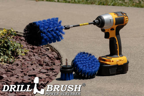 The Drillbrush 42J-5X Medium Blue Marine & Pool Brush Kit in a cordless drill sitting on a sidewalk next to a rock garden.