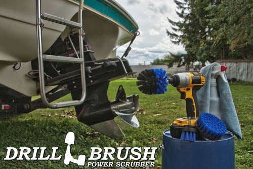 The Drillbrush 42O Medium Blue Marine & Pool Brush Kit in a cordless drill sitting on a bucket next to a spray bottle and rag in front of a boat on a trailer in a backyard.