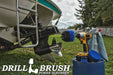 The Drillbrush 42O Medium Blue Marine & Pool Brush Kit in a cordless drill sitting on a bucket next to a spray bottle and rag in front of a boat on a trailer in a backyard.