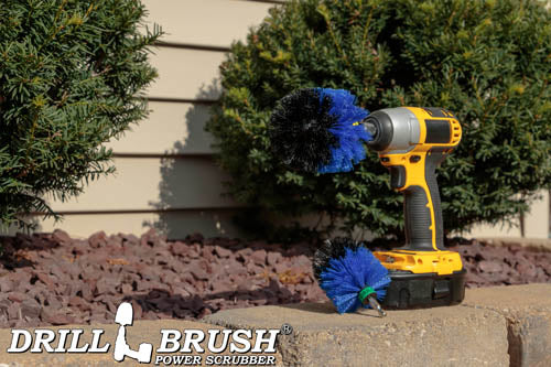 The Drillbrush MO Medium Blue Marine & Pool Brush Kit in a cordless drill sitting on a brck planter in front of a rock garden and some shrubs.