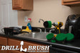The Drillbrush 542O Medium Green Kitchen Brush Kit in a cordless drill sitting on a kitchen counter in front of a sink, coffeemaker, and dishes.